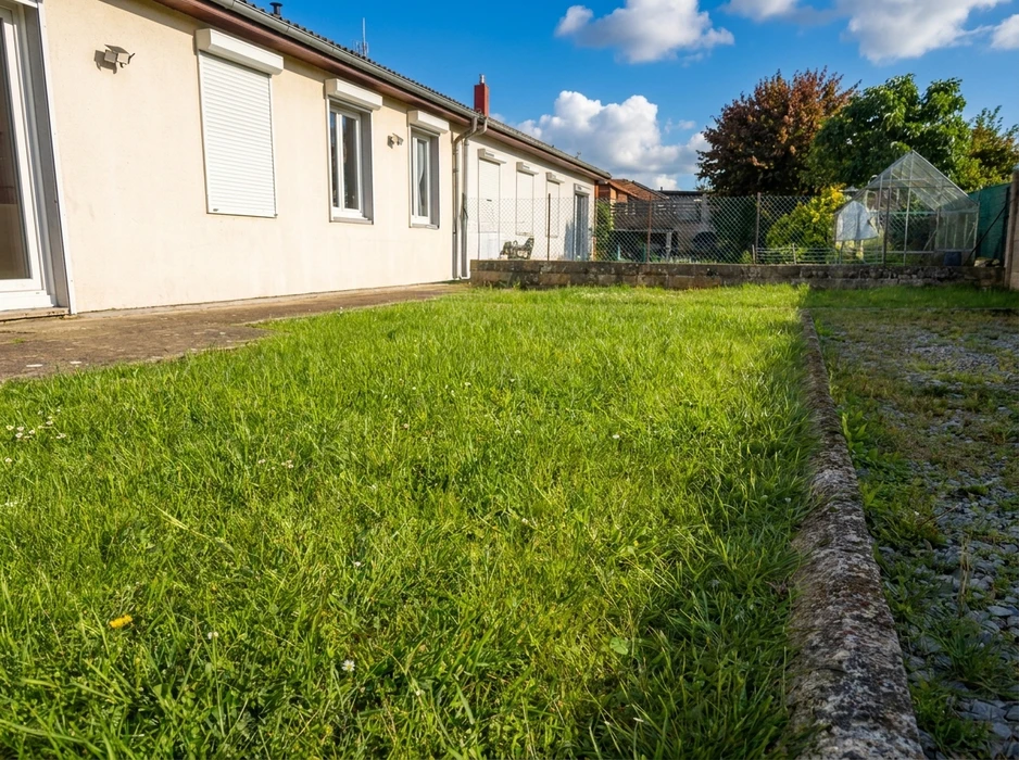 Jardin résidentiel extérieur, pelouse en gazon naturel non tondu, bordure en pierre de taille séparant la zone enherbée d'une allée gravillonnée